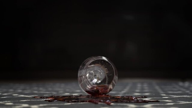Detail front view of unrecognizable male hand dropped glass of red wine on carpet on black background. Closeup cropped shot view of alcohol spilling on rug in living room. Shooting in slow motion.