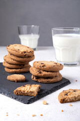 Close-up of baked oatmeal chocolate chip cookies on a slate serving board and milk in glasses. Selective focus. Vertical orientation.