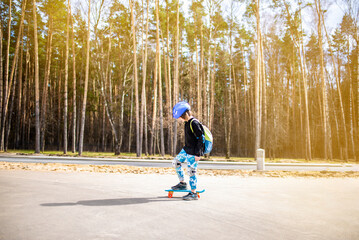 happy child schoolboy with a backpack goes to school on a skateboard. a joyful boy with protection on his knees and elbows, with a helmet on his head, stands on a plastic bright city cruiser skate