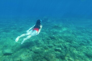 Girl swimming underwater in the sea. Girl in the red swim suit and shallow ocean with rocky seabed. Summer adventure, underwater picture from the snorkeling.