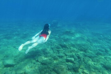 Girl swimming underwater in the sea. Girl in the red swim suit and shallow ocean with rocky seabed....