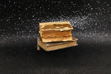 Two tattered old vintage books levitating on sparkling black glittery background. Photo with selective focus