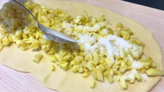 person sprinkles apples with spoon now they will bake apple strudel sugar is poured from tablespoon onto finely chopped on yeast dough
