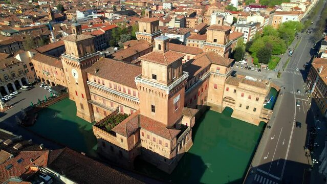 Aerial orbit of Castello Estense medieval castle in Ferrara, Italy. Drone rising to reveal historic city center with dense architecture around fortress and water moat. Panoramic 4k stock video.