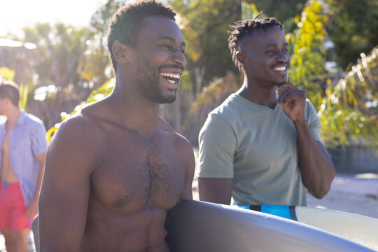 Happy african american male friends holding surfboards at beach