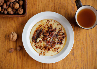 Healthy gluten free porridge cooked from buckwheat and corn semolina and served on white plate with cinnamon, maple syrup, butter and nuts. Top view porridge on wooden table.