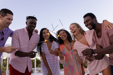 Happy diverse friends having party by swimming pool, holding sparklers