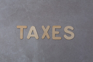 
Blond wood capital letters spelling the word TAXES against textured grey tile