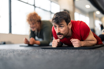 Focused young sports man fitness instructor on his limits looking exhausted doing plank session...