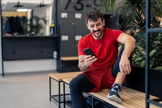 Handsome positive young sports man gym coach or client using smart phone fitness apps after workout tracking body wellness progress healthy lifestyle improvement while sitting in locker room.
