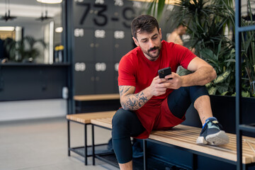 Handsome focused young sports man gym coach or client using smart phone technology fitness apps...