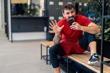 Fototapeta na wymiar Young motivated male athlete personal trainer at gym on mobile phone call, talking on loudspeaker, consulting client or having conversation with friend while sitting in locker room looking satisfied.