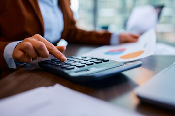 Close up of accountant using calculator while analyzing business reports in office.