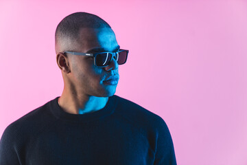 Serious black man in sunglasses looking to the side. Medium closeup studio shot over pink...