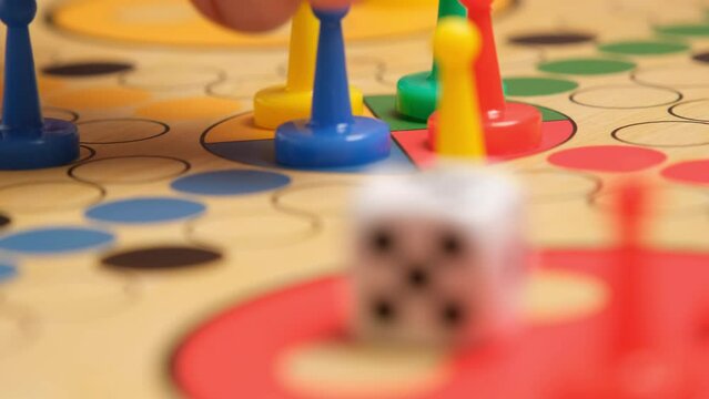 People play Ludo or Pachisi board game on beautiful wooden play board. Ludo is a strategy board game for two to four players. 4K resolution family board game video.