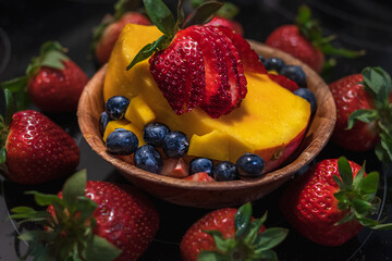 Wooden bowl with fresh fruits salad on dark background. Bowl of fruit salad with berries and mango