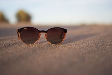 Fototapeta na wymiar Sunglasses resting on the sand of a dune with sunset light
