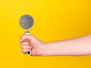 Pizza cutter in front of yellow background. Male hand, no face, copy space.
