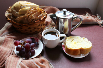 Brazilian breakfast. Coffee cup bread with butter grapes and bread in a wicker basket.