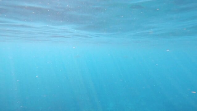 Underwater slow motion shot of sun rays shining through the surface of the clear blue peaceful ocean