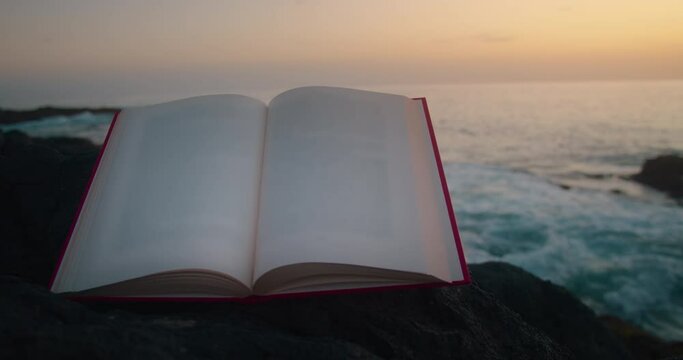 Blank pages of an open red book on the background of the ocean at sunset.