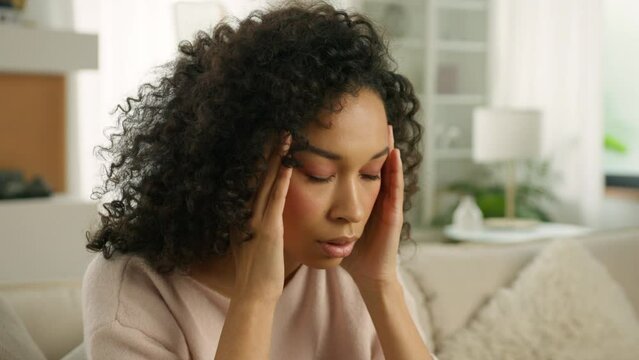 Close up face sad thoughtful young African American single woman looking away thinking of problems. Woman of color siting on sofa alone at modern home troubled with negative thought in slow motion 4K