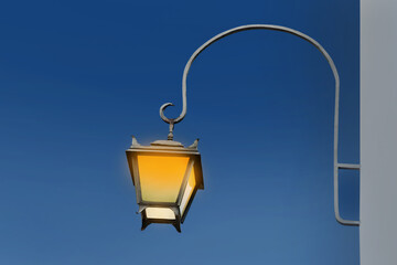 Fototapeta na wymiar Turned on hanging street lamp in old fashion style on building