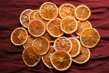 Heap of dry orange slices on burgundy fabric, flat lay