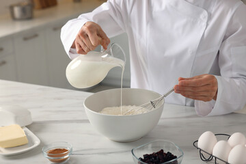 Professional chef adding milk into dough at white marble table indoors, closeup