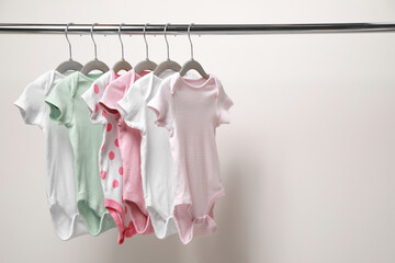 Baby bodysuits hanging on rack near white wall. Space for text