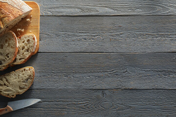 Obraz na płótnie Canvas Food photography. Cut freshly baked bread and knife on wooden table, flat lay with space for text