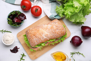 Delicious sandwich with salmon and ingredients on white table, flat lay
