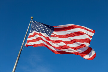Close up view of an American flag waving on a flagpole, with blue sky background and copy space
