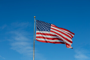 Close up view of an American flag waving on a flagpole, with blue sky background and copy space
 - Powered by Adobe
