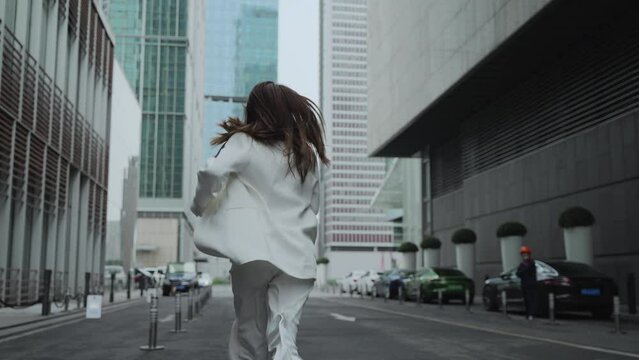 Close up of back of woman in white suit running in street surrounded by building in morning . Chinese female running in city symbols the positive life attitude to life and work.