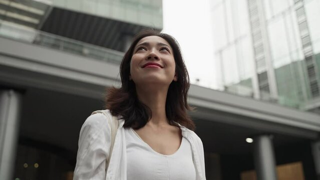 Close up of woman in white looking up sky in street surrounded by building in morning . Chinese female look up sky  in city symbols the positive life attitude to life and work.