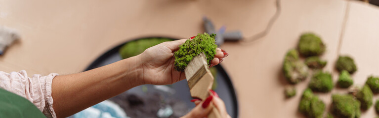Close up of woman decorator making green ikebana on tray with epoxy resin in florist workshop