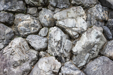 Background of large coarse gray rocks forming a wall. Frontal view of a gray rock wall.