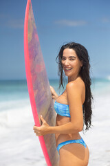 Happy young beautiful girl with a surfboard on the beach in the summertime in Hawaii