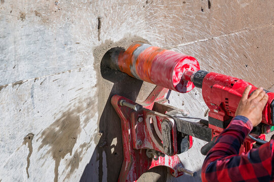 Worker is drilling to concrete wall with core drill machine. core drill is a drill specifically designed to remove a cylinder of material, much like a hole saw. The material left inside the drill bit.