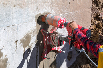 Worker is drilling to concrete wall with core drill machine. core drill is a drill specifically designed to remove a cylinder of material, much like a hole saw. The material left inside the drill bit. - obrazy, fototapety, plakaty