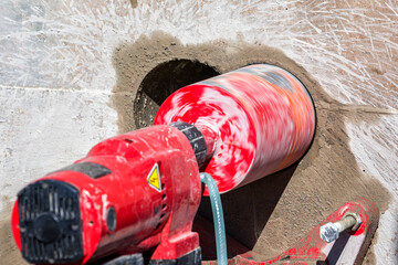 Worker is drilling to concrete wall with core drill machine. core drill is a drill specifically designed to remove a cylinder of material, much like a hole saw. The material left inside the drill bit. - obrazy, fototapety, plakaty
