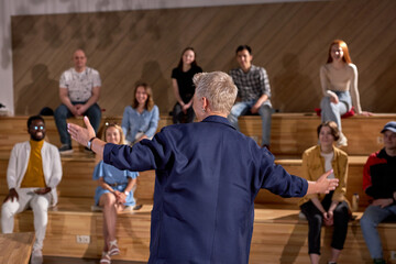 View from back on nice short haired female speaker in formal suit giving speech to adult people during seminar in conference lecture hall. rear view. focus on woman spreading arms while talking