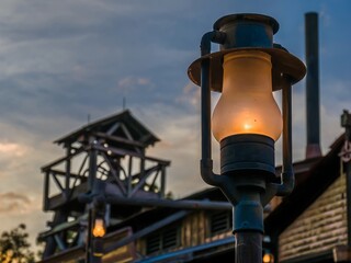 Old mining lantern on a lamppost in front of old mining camp during sunset