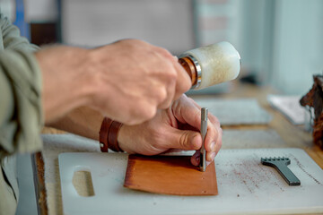 young man's hands punching holes in the leather with a punch.Tools for leather craft.side view