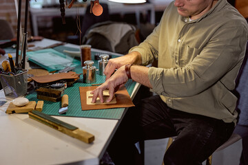 young man in green T-shirt cutting leather material, close up cropped side view shot