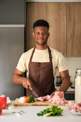 Young black man smiling and looking at camera while de-boning chicken to prepare a recipe in a kitchen.
