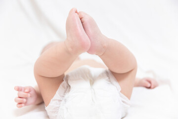 A asian korean baby with a diaper on a white cloth background is lying down, stretching his legs...