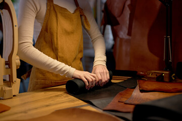 skilled female tailor unwrapping roll of leather on table in workshop at home.close up cropped side view shot