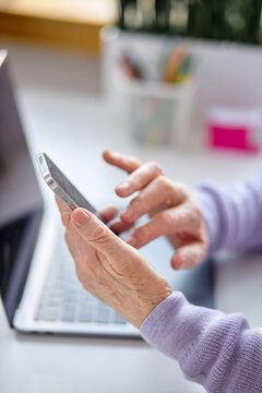 Cropped senior woman using smartphone checking email news online sitting in living room, searching for friends in internet social networks or working on computer, writing blog